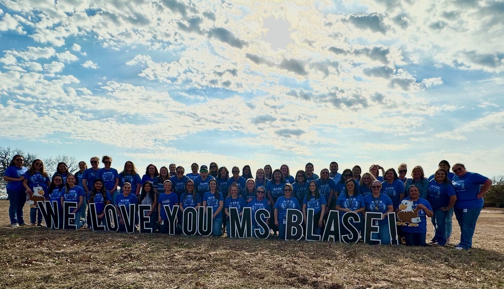 rann staff in blue shirts standing behind yard sign that says "we love you ms. blase"